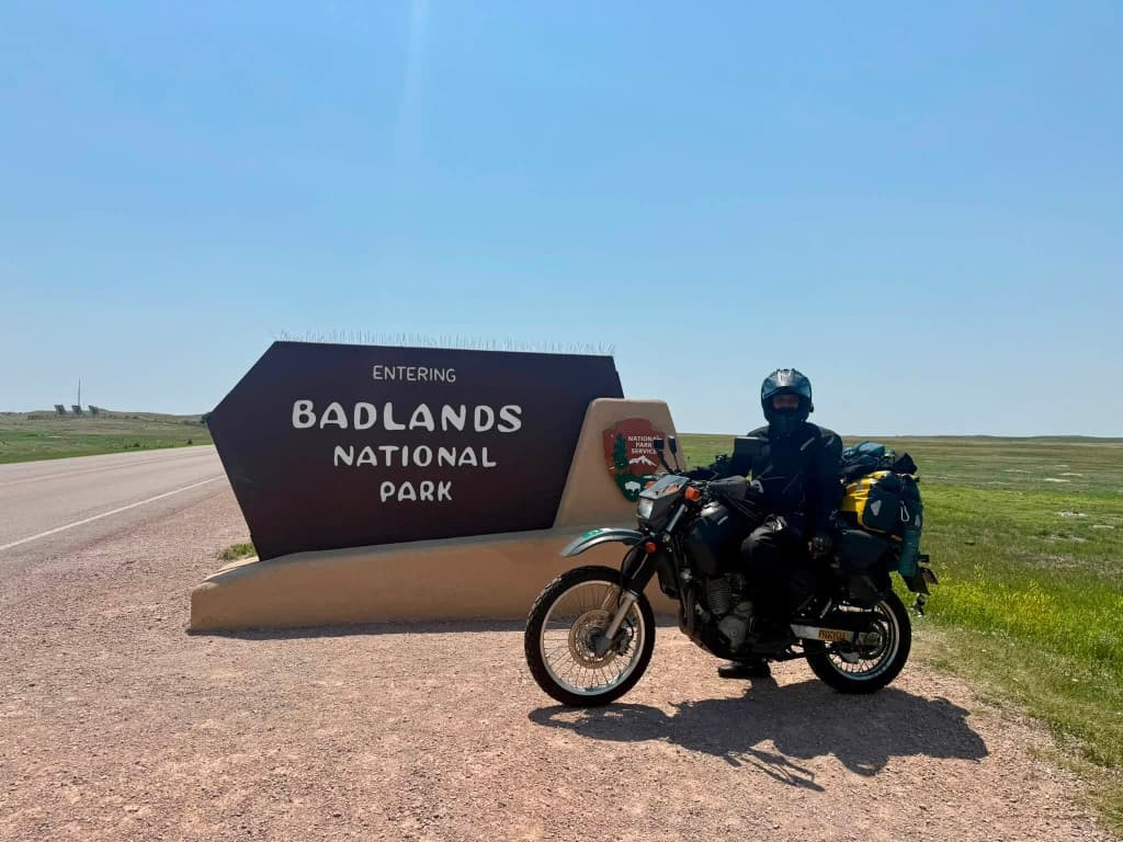 Rider on loaded DR650 at Badlands National Park entrance sign