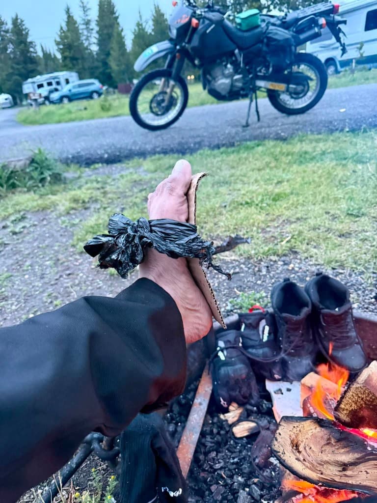 Campfire drying boots with makeshift cardboard sole after gear failure